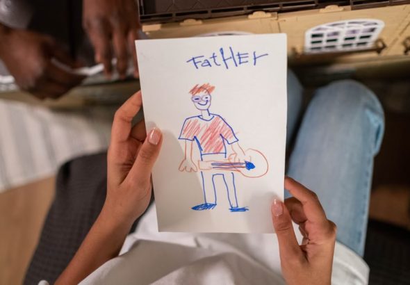 A high-angle view of a child's drawing of their father, placed in front of a toy house, showing family creativity.