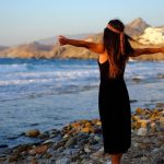 Woman enjoying freedom at sunset on a rocky beach in Greece.