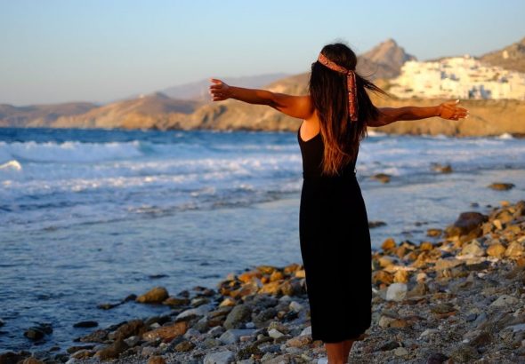 Woman enjoying freedom at sunset on a rocky beach in Greece.