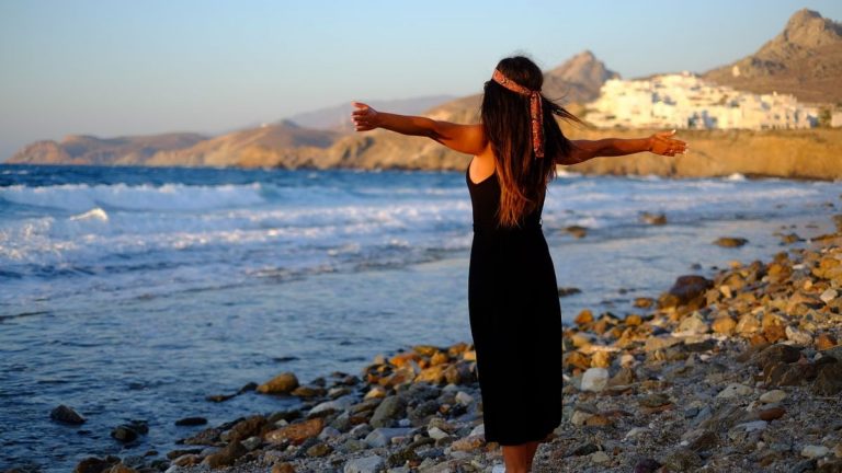 Woman enjoying freedom at sunset on a rocky beach in Greece.