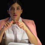Woman in pink blazer sitting at a desk with papers under lamp light.