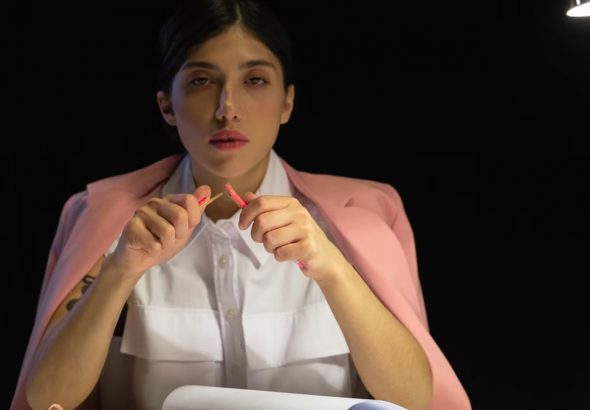 Woman in pink blazer sitting at a desk with papers under lamp light.