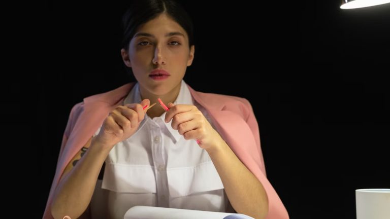 Woman in pink blazer sitting at a desk with papers under lamp light.